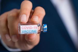 Focus select and blur Foreground Vaccine COVID-19 corona virus and syringe on hand business man in blue suit background. Concept of attentive care. photo