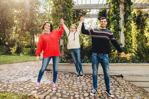 una mujer muy joven usa suéter rojo y jeans, un hombre guapo mantiene a su pequeña hija con las manos, trata de balancearla, pasa un tiempo maravilloso e inolvidable juntos al aire libre. concepto de unión. foto