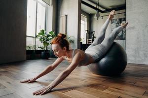 Young ginger sportive woman doing stretching exercises on stability exercise ball photo