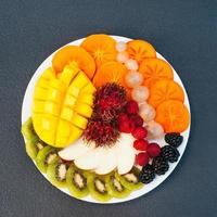 Slices of ripe exotic fruits on white plate. Kiwi, mango, raspberry, blueberry and persimmon. Fruits assortment. Top view. Healthy diet concept
