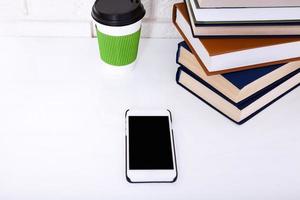 Education workplace with books, cup of coffee and mobilephone on white table near brick wall. Selective focus photo