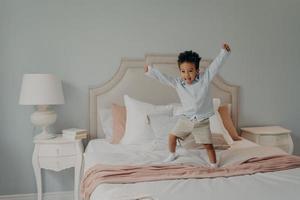Adorable cute kid jumping cheerfully on bed and having fun at home photo