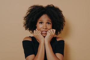 Scared mixed race female looking nervously and feeling stress while posing against beige background photo