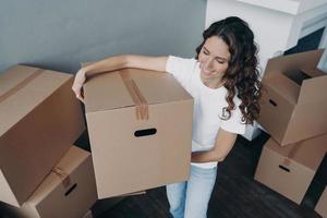 Woman is moving to better place and carrying box. Happy european lady purchasing real estate. photo