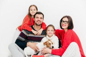 Portrait of happy family members with positive expressions, cuddle and support each other, have good relationship. Delighted father, mother, two sisters and small puppy pose together indoor. photo