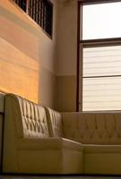 Old cream-colored sofa in the corner of the room with window light. photo