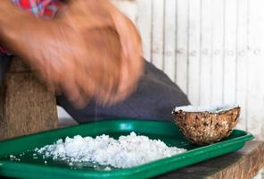 anciano con los dedos para raspar el coco en la bandeja. foto