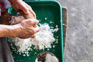 anciano con los dedos para raspar el coco en la bandeja. foto