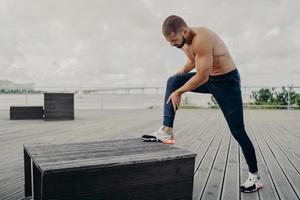 atleta masculino sufre de dolor en las piernas, toca el tobillo después de torcerlo y hace ejercicio al aire libre, usa pantalones deportivos, zapatillas de deporte. el deportista tiene una lesión muscular durante el trote al aire libre. concepto de accidente foto