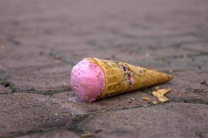 Strawberry ice cream falling on a street sidewalk and a broken waffle cone photo