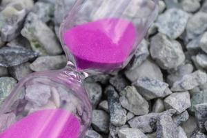 Hourglass with pink sand on small stones, symbol of time photo