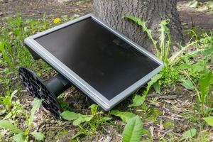 A faulty monitor is lying on the street under a tree in the grass photo