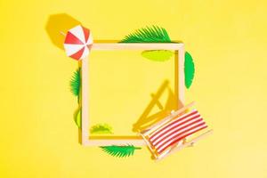 Wooden frame with beach chair and umbrella and tropical leaves with copy space top view photo