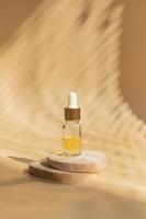 Glass bottle with a pipette on a wooden podium in the shade of blinds photo