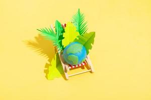 Beach chair with planet and tropical leaves on a yellow background. Global warming minimalist concept photo