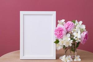 Empty white frame mock up with flowers on pink background. Temlate for your text or picture photo