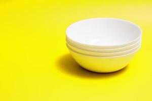 Four white empty soup plates on a yellow background with copy space. Food, cooking, kitchen concept photo