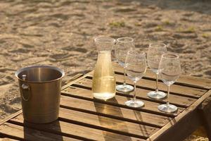 bottle of wine, glasses and ice on wooden table, summer beach background photo