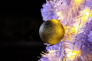 primer plano del árbol de navidad blanco con la bola de oro colgando decoraciones con luces doradas brillantes. foto