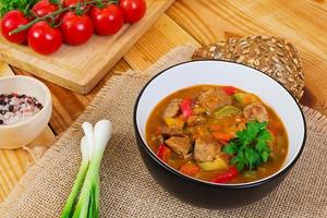 Stew with meat and vegetables in tomato sauce on wooden background photo