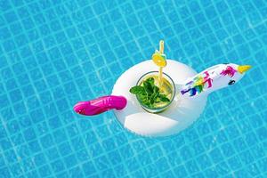 Fresh coctail mojito on inflatable white unicorn toy at swimming pool. Vacation concept.