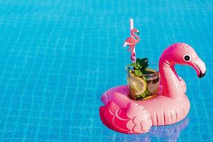Fresh coctail mojito on inflatable pink flamingo toy at swimming pool. Vacation concept.