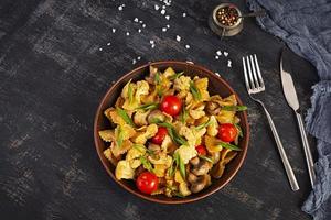Stir fry farfalle pasta with vegetables, cauliflower and mushrooms. Top view photo
