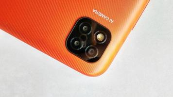 Orange smartphone with Artificial Intelligence cameras under white gray background. Suitable for company and industry advertising, poster, backdrop, promotion, tech company, etc. photo