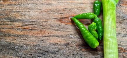 Vegetables of leek, garlic, and green chilli on the wooden cutting board. Vegetables ingredient background design. Suitable for advertising of food, drink, poster, backdrop, food company and industry. photo
