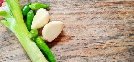 Vegetables of leek, garlic, and green chilli on the wooden cutting board. Vegetables ingredient background design. Suitable for advertising of food, drink, poster, backdrop, food company and industry. photo
