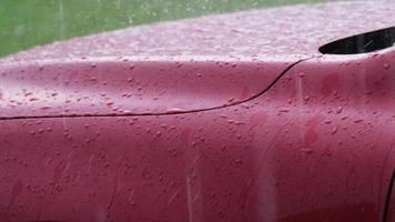 close-up em câmera lenta da chuva caindo e os pingos de chuva saltando no capô do carro vermelho. a chuva caía no capô do carro vermelho. vista lateral