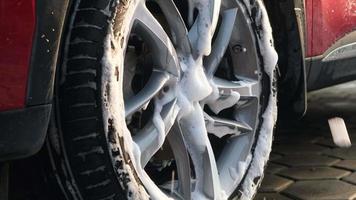 Manual car wash with sponge and soap, foam flowing on the alloy wheels of a car. Car wash service concept. video