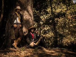 A twin senior cowboy stand and sat with a gun to guard the safety of the camp in the western area photo