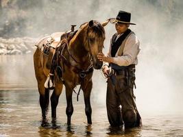 un joven vaquero descansó con un caballo en el arroyo después de que terminó de duchar al caballo foto