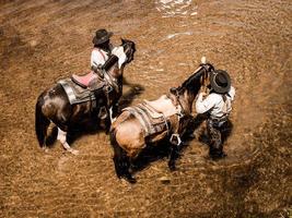 Old and young cowboys rest with their horses in the stream after they finish bathing photo