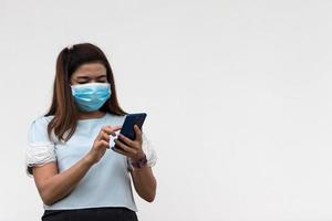 A woman wearing a mask with a mobile phone near a concrete wall. photo