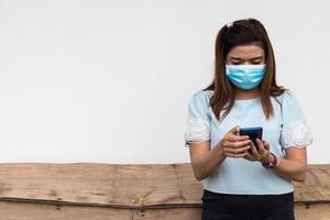 A woman wearing a mask with a mobile near an old wooden table. photo