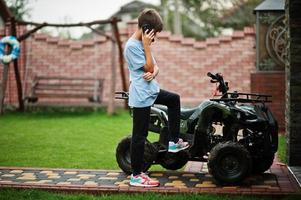 niño en cuatriciclo atv de cuatro ruedas con teléfono móvil. foto