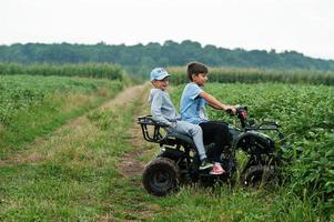 Two brothers driving four-wheller ATV quad bike. Happy children moments. photo