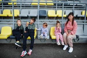 joven madre elegante con cuatro hijos sentados en sillas en el estadio. la familia pasa tiempo libre al aire libre. foto