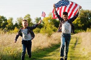 dos hermanos corriendo con la bandera de estados unidos. vacaciones de américa. orgullosos de ser hijos de patria. foto