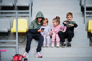 Four cuttie kids sitting on sport area and looking at mobile phone. photo