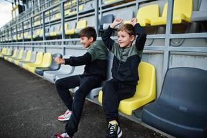 Two brothers support their favorite team, sitting on the sports podium at the stadium. photo