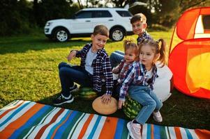 cuatro niños pasando tiempo juntos. manta de picnic al aire libre, sentada con sandías. foto