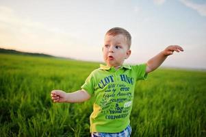 Cute boy in green grass field at evening. photo