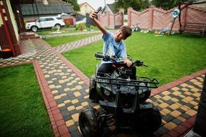 niño en cuatriciclo atv de cuatro ruedas con teléfono móvil. foto