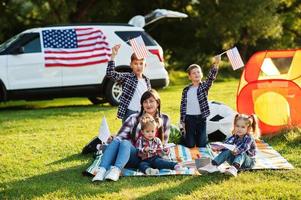 American family spending time together. With USA flags against big suv car outdoor. photo