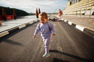 Baby girl running. Sports family spend free time outdoors with scooters and skates. photo