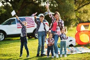 American family spending time together. With USA flags against big suv car outdoor. photo