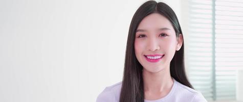 Portrait of beautiful young Asian woman posing, happy smiling, look at camera.  Teenager Asian lady girl wearing casual shirt, facial lip pretty. While relaxing indoor bedroom at home with copy space. photo